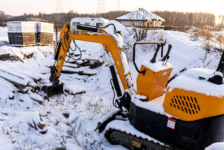 Mini excavator resting in snow on winter construction site
